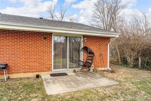 exterior space with a patio area, roof with shingles, a yard, and brick siding