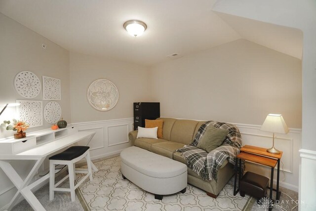 living area with lofted ceiling, a decorative wall, and wainscoting