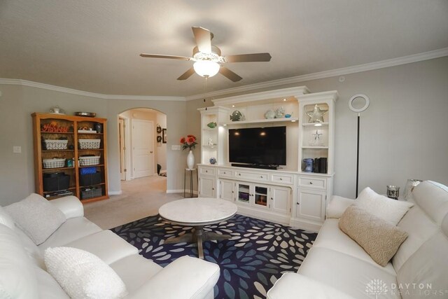 living room with light carpet, arched walkways, baseboards, ceiling fan, and ornamental molding