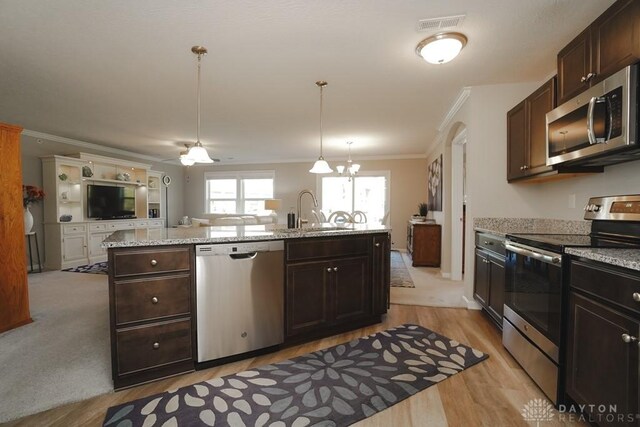 kitchen featuring stainless steel appliances, a sink, open floor plan, decorative light fixtures, and crown molding