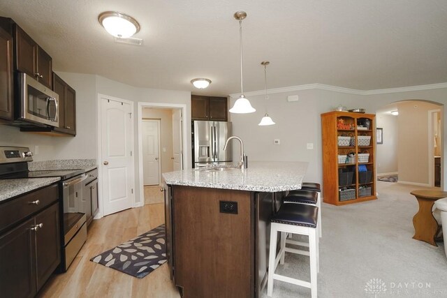 kitchen featuring a center island with sink, arched walkways, a breakfast bar area, stainless steel appliances, and a sink