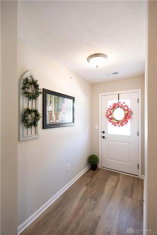 doorway to outside featuring a textured ceiling, wood finished floors, visible vents, and baseboards