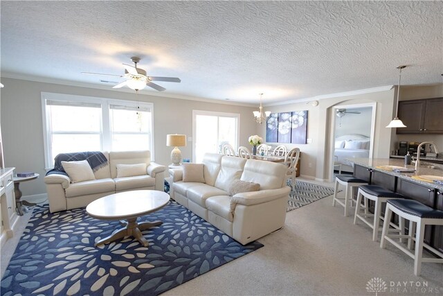 living room with light carpet, ornamental molding, and ceiling fan with notable chandelier