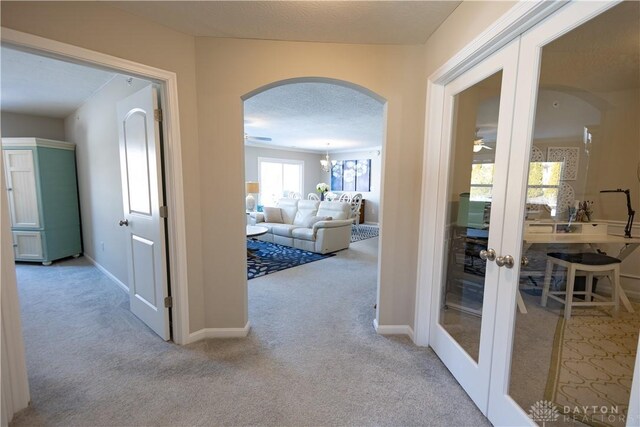 corridor featuring baseboards, arched walkways, light colored carpet, a textured ceiling, and french doors