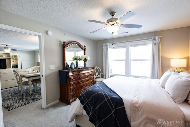 bedroom with baseboards, visible vents, a ceiling fan, light colored carpet, and a textured ceiling