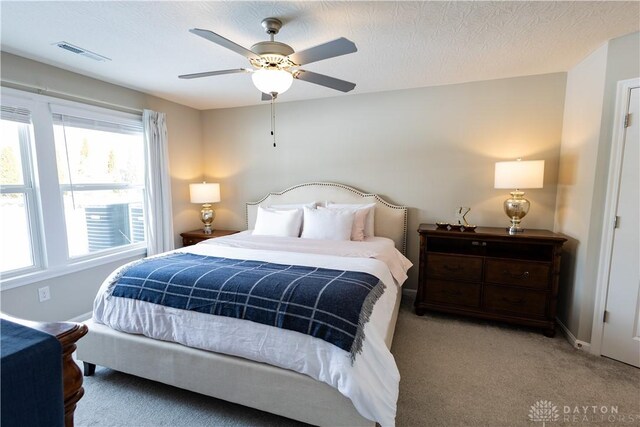 bedroom featuring light colored carpet, visible vents, a ceiling fan, a textured ceiling, and baseboards