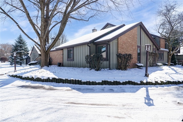 snow covered property with brick siding, board and batten siding, and a chimney