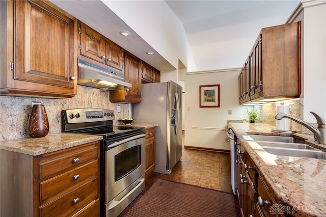 kitchen with baseboards, appliances with stainless steel finishes, light stone countertops, under cabinet range hood, and a sink