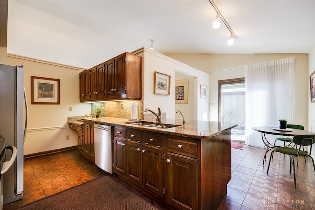 kitchen featuring stainless steel appliances, stone counters, a peninsula, and a sink