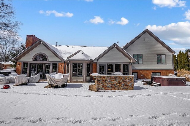 snow covered property with a chimney, brick siding, and a hot tub