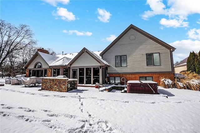 snow covered property featuring a chimney, brick siding, and a hot tub