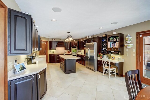 kitchen with decorative light fixtures, light countertops, custom range hood, appliances with stainless steel finishes, and an island with sink