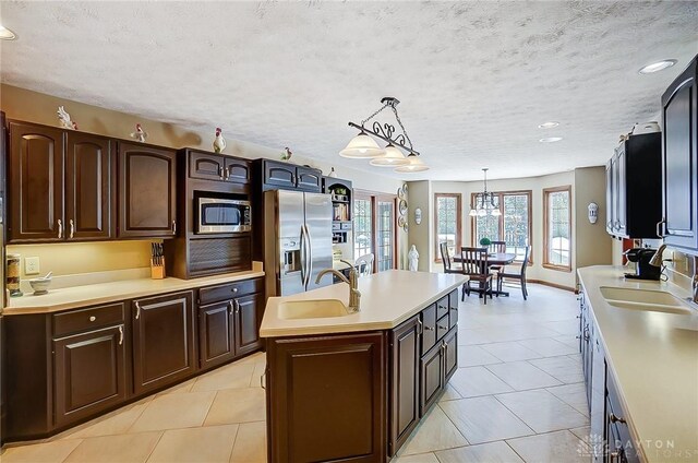 kitchen with decorative light fixtures, a center island with sink, stainless steel appliances, light countertops, and a sink