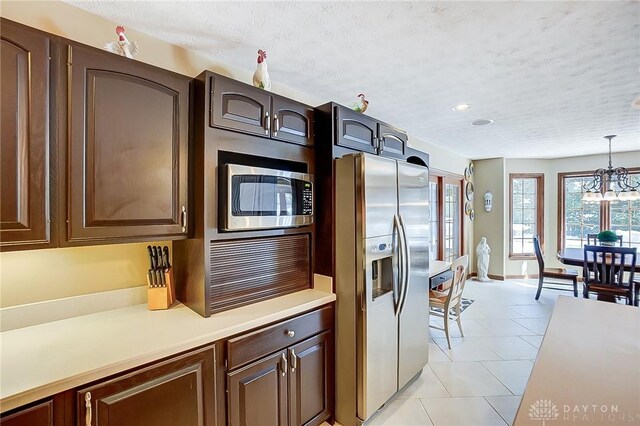 kitchen with a textured ceiling, light tile patterned floors, light countertops, appliances with stainless steel finishes, and hanging light fixtures