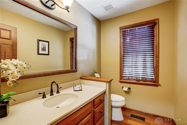 half bathroom with toilet, visible vents, wood finished floors, and vanity