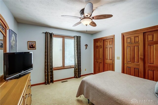 bedroom with baseboards, multiple closets, visible vents, and light colored carpet