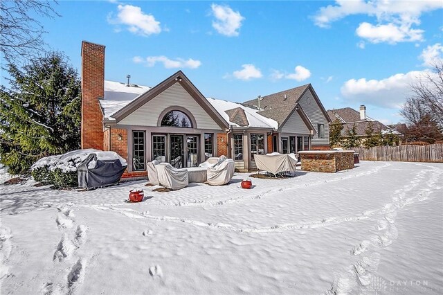 snow covered house with french doors, brick siding, fence, and a chimney