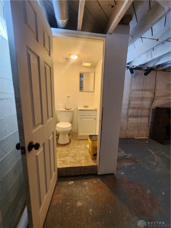 bathroom featuring a sink, toilet, and concrete block wall