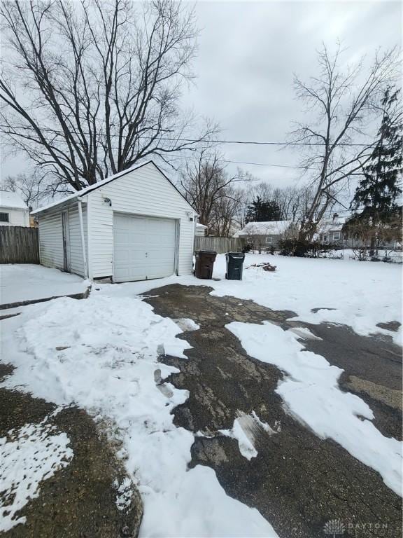 snowy yard featuring a detached garage, fence, and an outbuilding