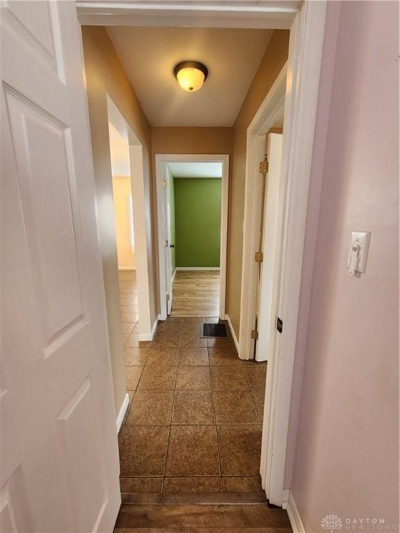 hallway with dark tile patterned floors, visible vents, and baseboards