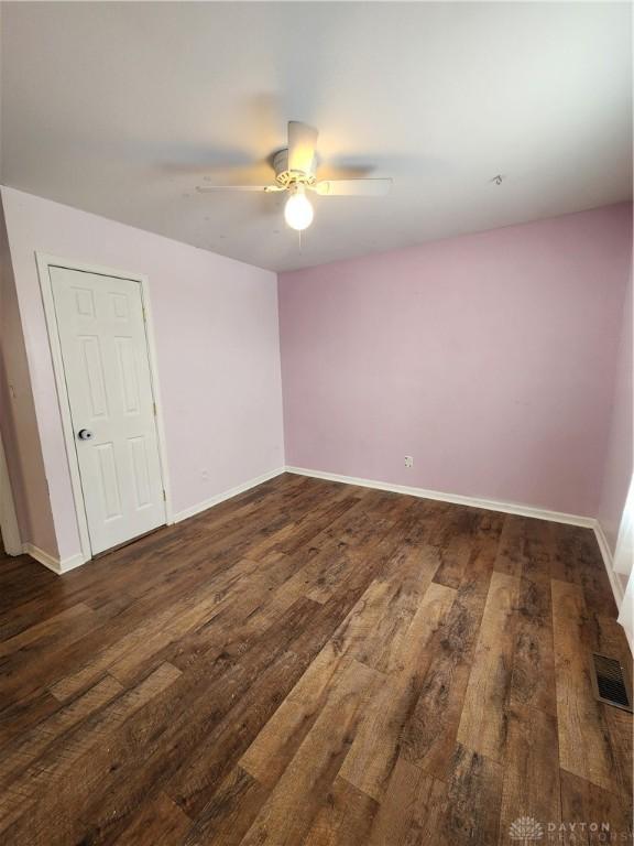 spare room with a ceiling fan, visible vents, dark wood finished floors, and baseboards