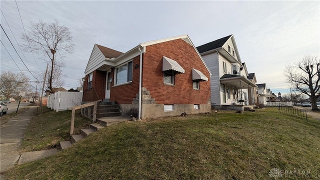 view of side of property featuring fence, a lawn, and brick siding