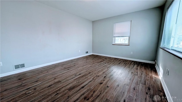 unfurnished room featuring dark wood-style flooring, visible vents, and baseboards