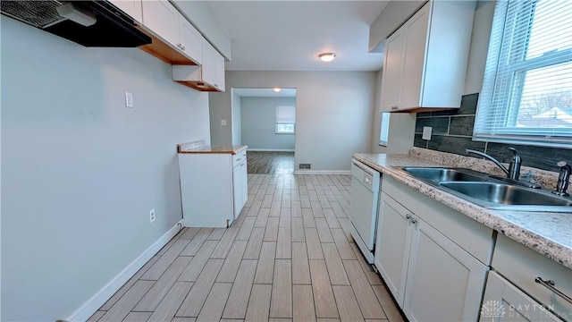 kitchen featuring white cabinets, dishwasher, backsplash, light countertops, and a sink