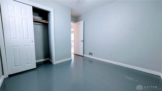 unfurnished bedroom featuring dark wood-style floors, a closet, visible vents, and baseboards