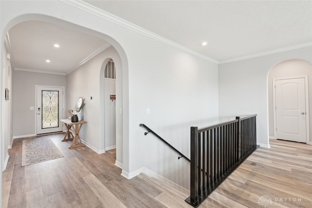 corridor featuring arched walkways, light wood-type flooring, baseboards, and crown molding