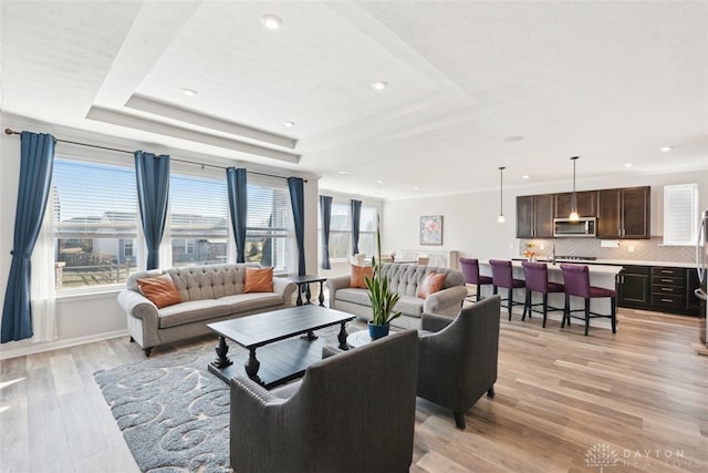 living room featuring a tray ceiling, crown molding, recessed lighting, light wood-style floors, and baseboards