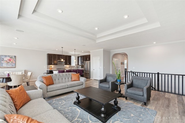 living area featuring arched walkways, a tray ceiling, light wood finished floors, and crown molding