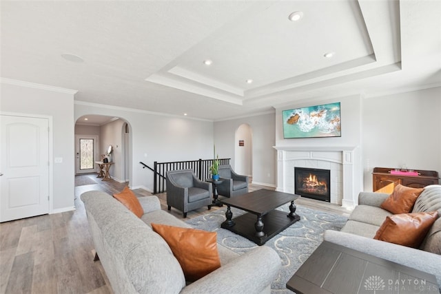 living area with a tray ceiling, a fireplace, arched walkways, and light wood finished floors