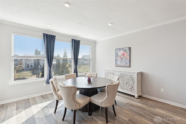 dining room with baseboards, a textured ceiling, ornamental molding, and wood finished floors