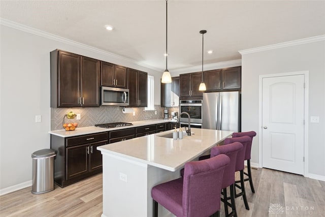 kitchen featuring a center island with sink, stainless steel appliances, light countertops, pendant lighting, and a sink