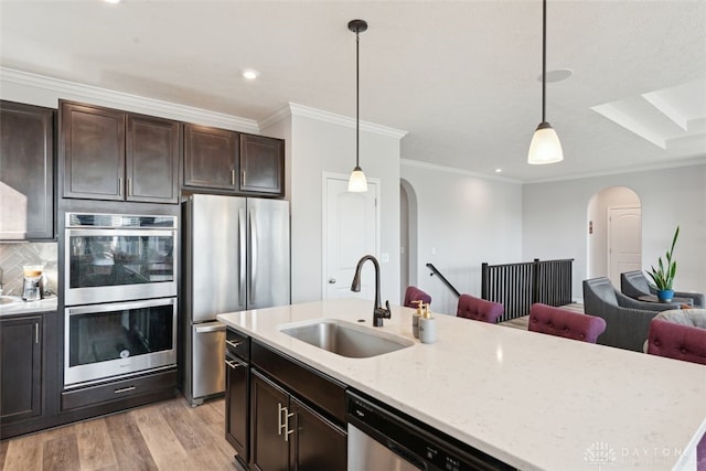 kitchen featuring open floor plan, stainless steel appliances, hanging light fixtures, and a sink