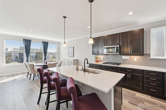 kitchen with appliances with stainless steel finishes, hanging light fixtures, a kitchen island with sink, a kitchen bar, and a sink