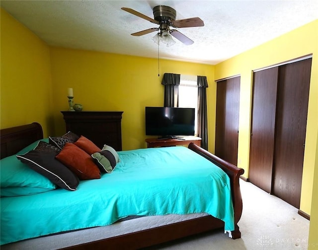 bedroom featuring a textured ceiling, carpet flooring, two closets, and a ceiling fan