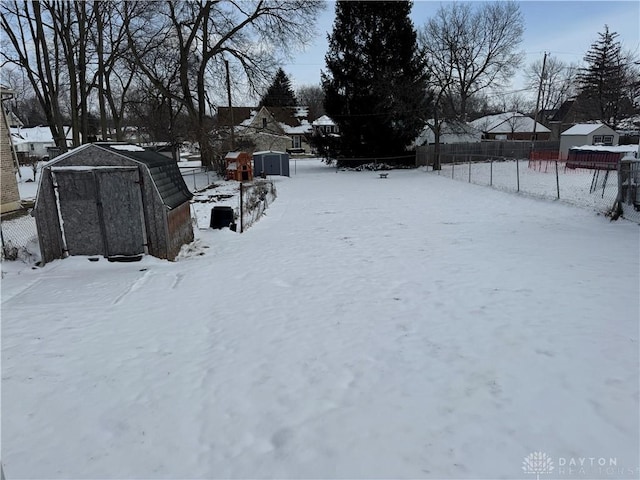 yard layered in snow featuring an outbuilding, fence, a residential view, and a storage unit