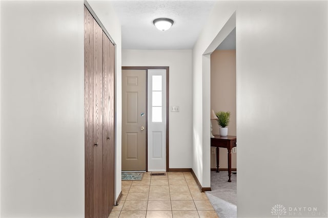 foyer entrance featuring a textured ceiling, baseboards, and light tile patterned floors