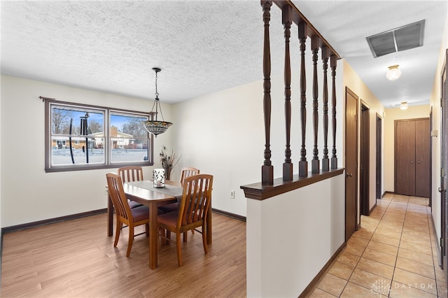 dining room featuring light wood-style floors, visible vents, a textured ceiling, and baseboards