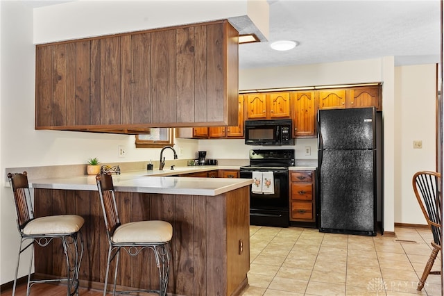 kitchen featuring brown cabinets, a breakfast bar area, light countertops, a peninsula, and black appliances