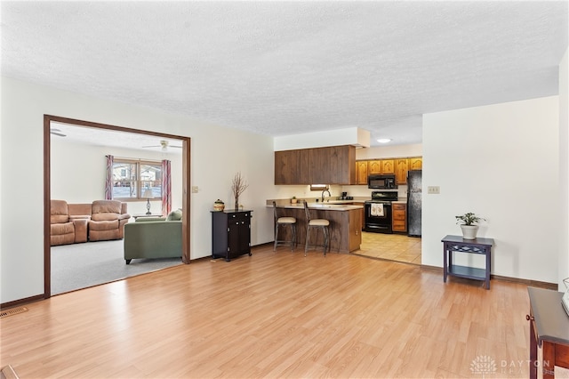 kitchen with open floor plan, black appliances, a peninsula, and a kitchen breakfast bar