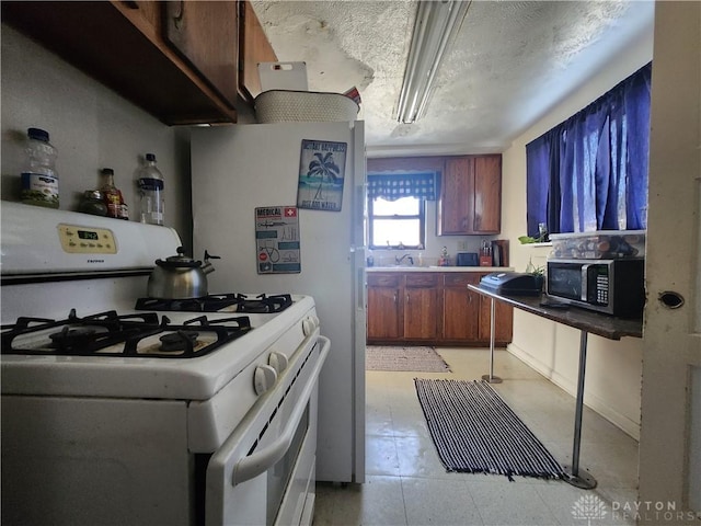 kitchen featuring stainless steel microwave, a sink, a textured ceiling, and white gas range