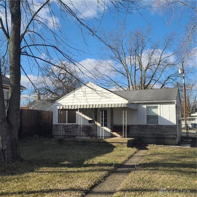 bungalow-style home with a shingled roof, stone siding, fence, a front lawn, and board and batten siding