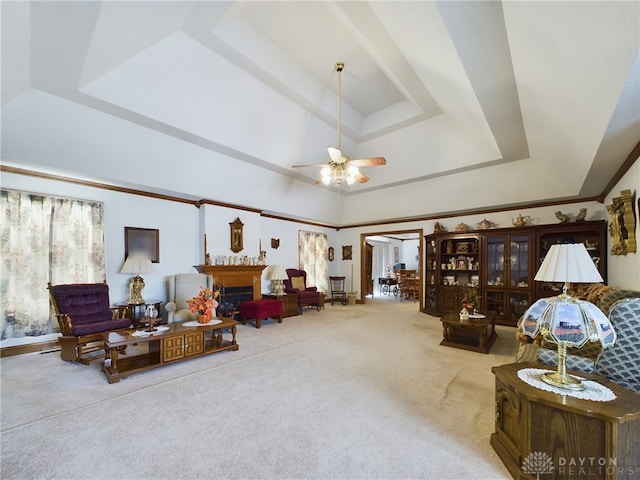 living area featuring ceiling fan, ornamental molding, a tray ceiling, carpet flooring, and a fireplace