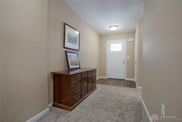 doorway to outside featuring a textured ceiling, carpet, and baseboards