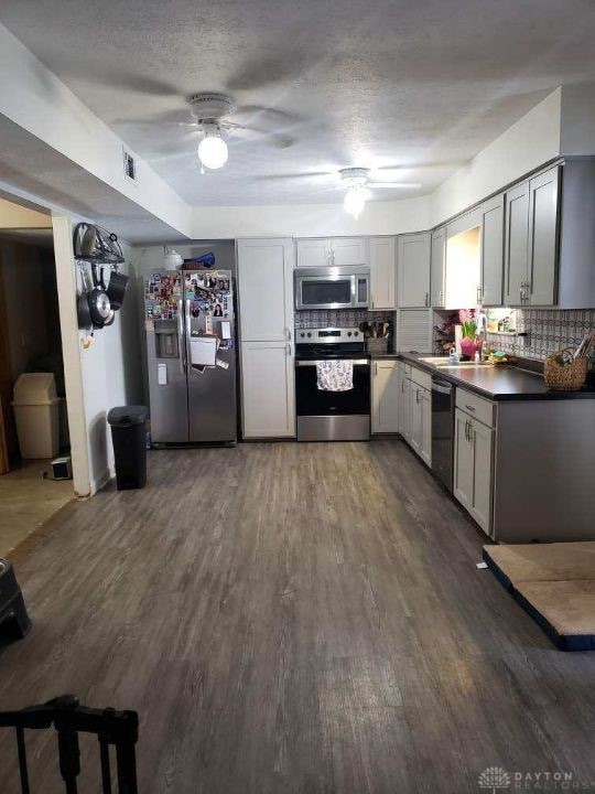 kitchen with dark wood finished floors, dark countertops, backsplash, gray cabinetry, and appliances with stainless steel finishes