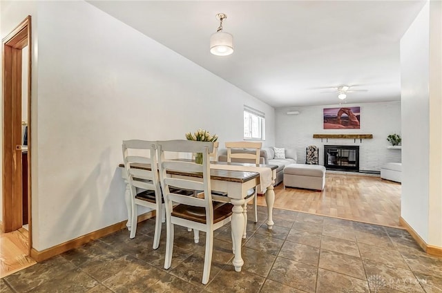 dining room featuring a brick fireplace, ceiling fan, and baseboards