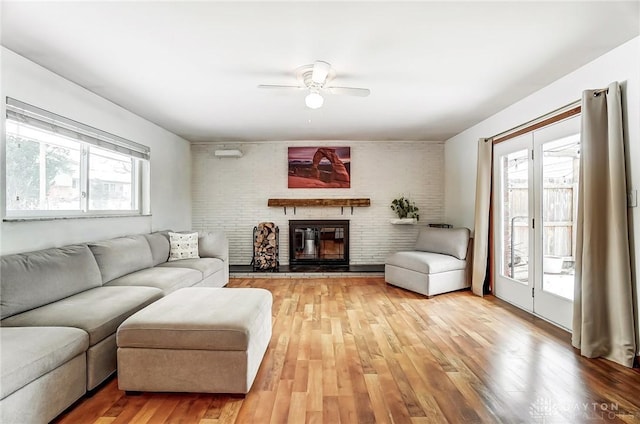 living area with ceiling fan, brick wall, a brick fireplace, and wood finished floors